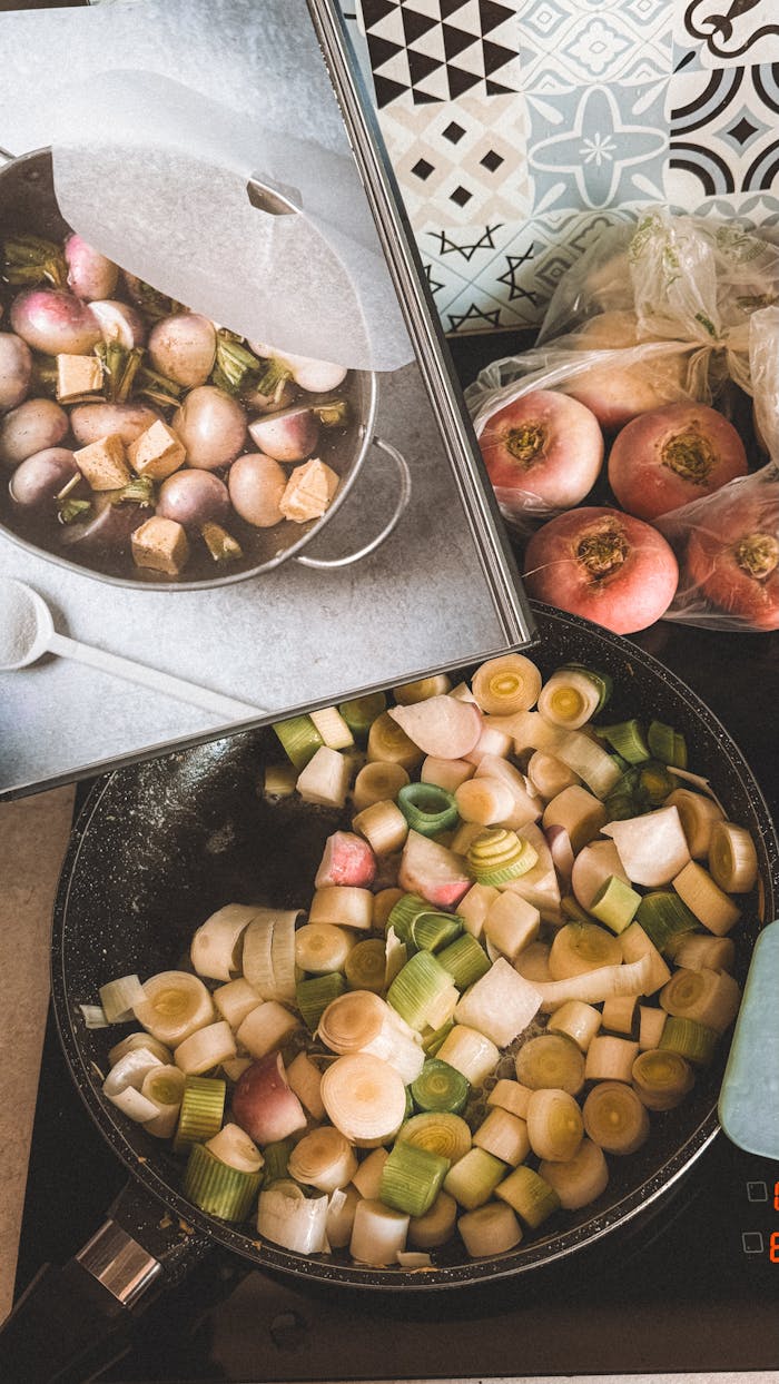 Services Top view of turnips and leeks cooking in a pan, with a cookbook for guidance.