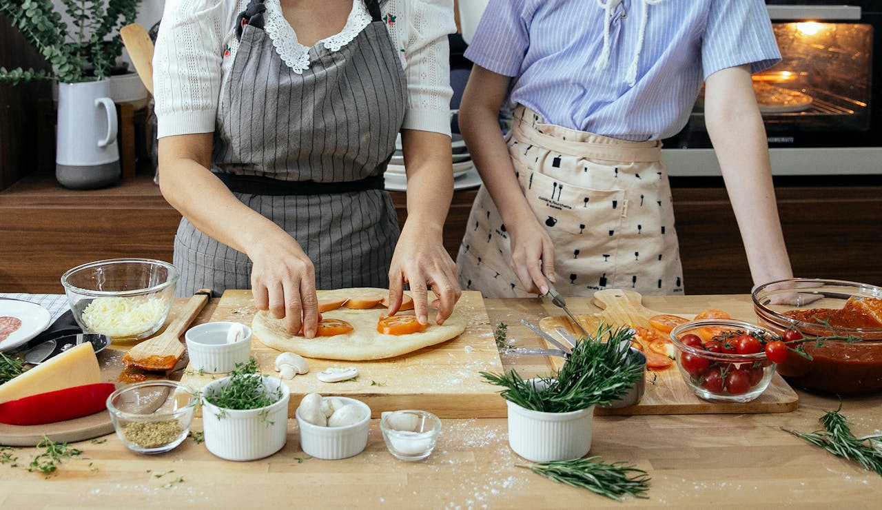 A bonding moment of mother and daughter preparing a homemade pizza with fresh ingredients.